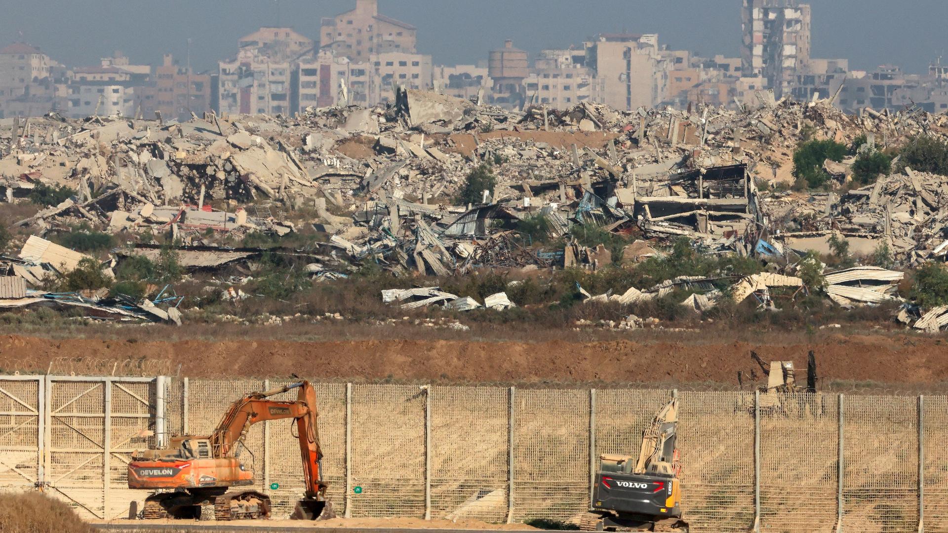 Israelische Bagger am Grenzzaun zum Gazastreifen. Im Hintergrund sind zerstörte Häuser.