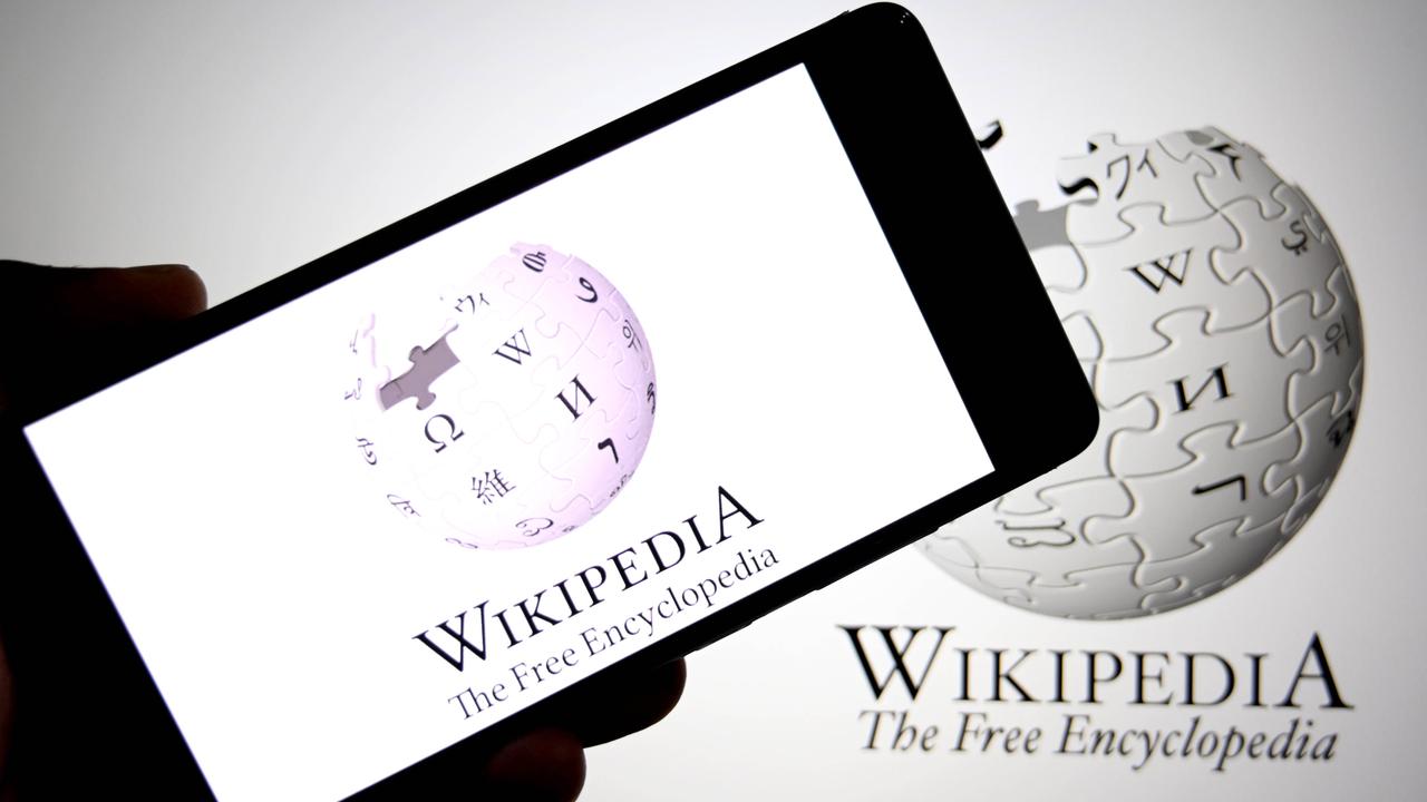Ein Foto auf dem eine Hand ein Smartphone mit Wikipedia auf dem Display vor einem Bildschirm mit Wikipedia auf dem Displaz hält.