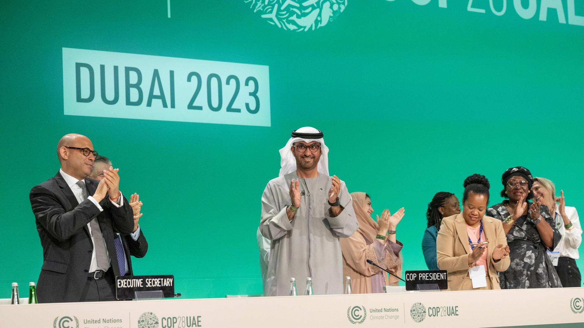 COP-Präsident Al Jaber steht klatschend auf dem Podium zum Abschluss der Weltklimakonferenz 2023 in Dubai. 