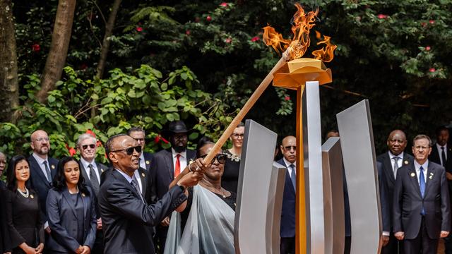 Der ruandische Präsident Kagame (links) and seine Ehefrau Jeannette Kagame entzünden die "Flamme der Erinnerung" auf einem großen Denkmal zum Genozid vor 30 Jahren. Dahinter andere Gäste der Gedenkenfeier.
