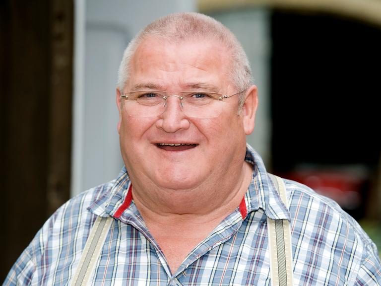 Schauspieler Horst Krause im karierten Hemd lächelt bei Dreharbeiten des Fernsehfilms "Krauses Braut" in die Kamera.