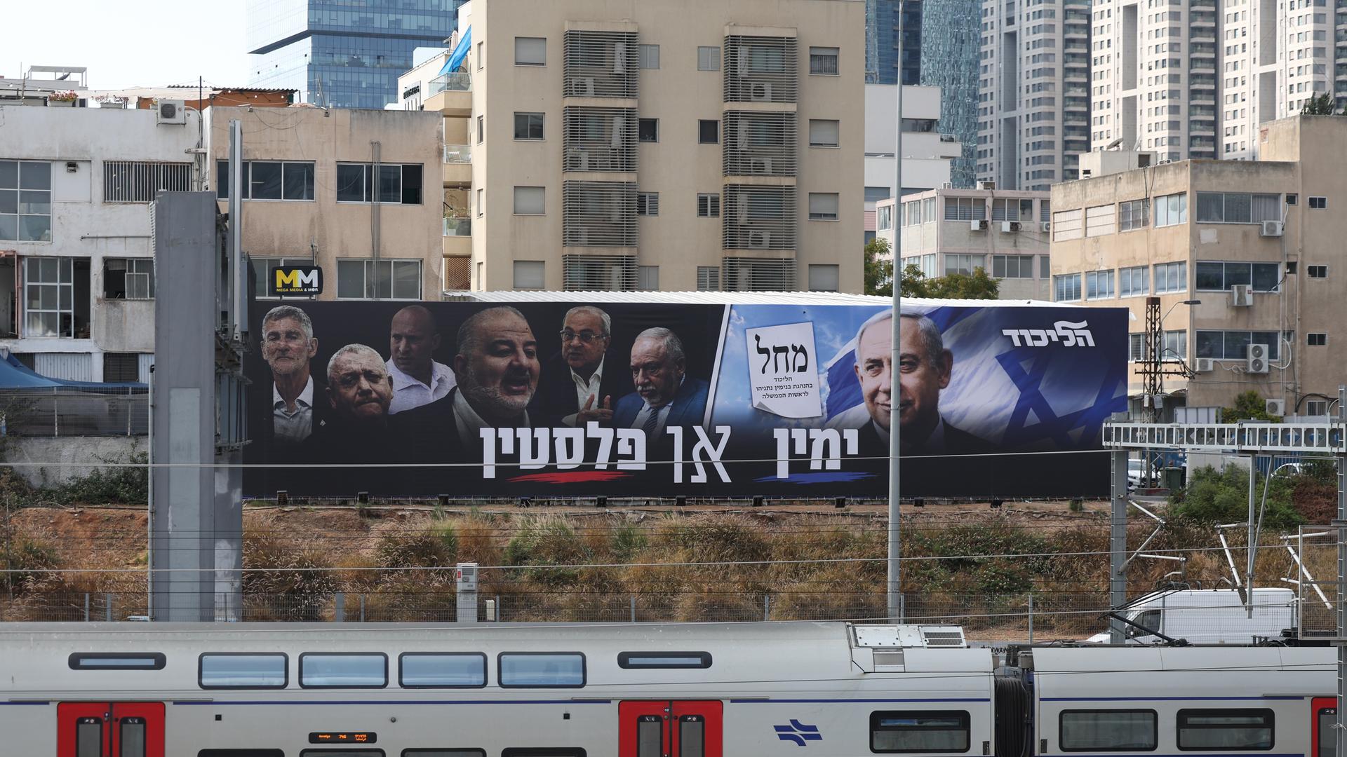 Zwei große Plakate mit Politikern hängen über einer Zugstrecke.