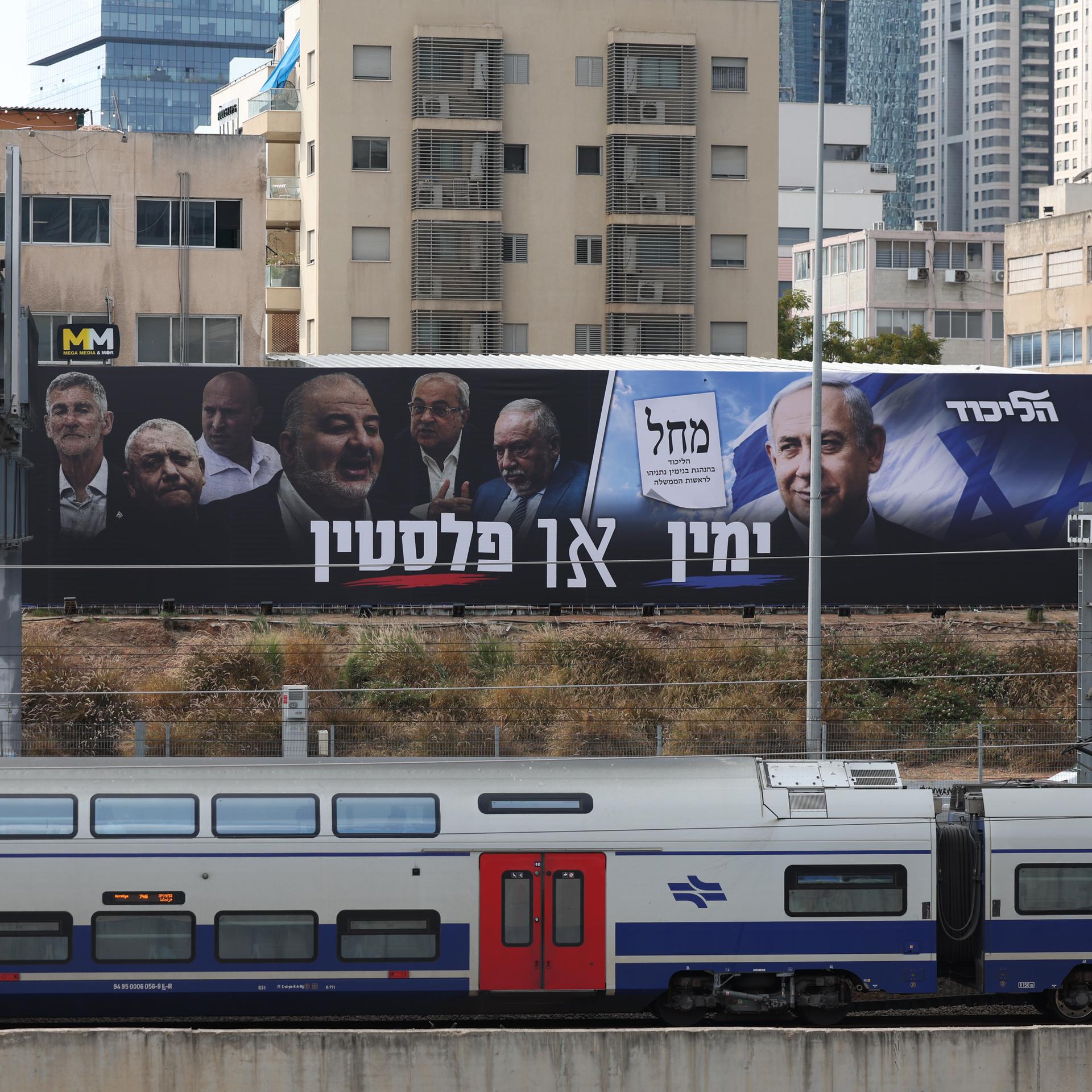 Zwei große Plakate mit Politikern hängen über einer Zugstrecke.
