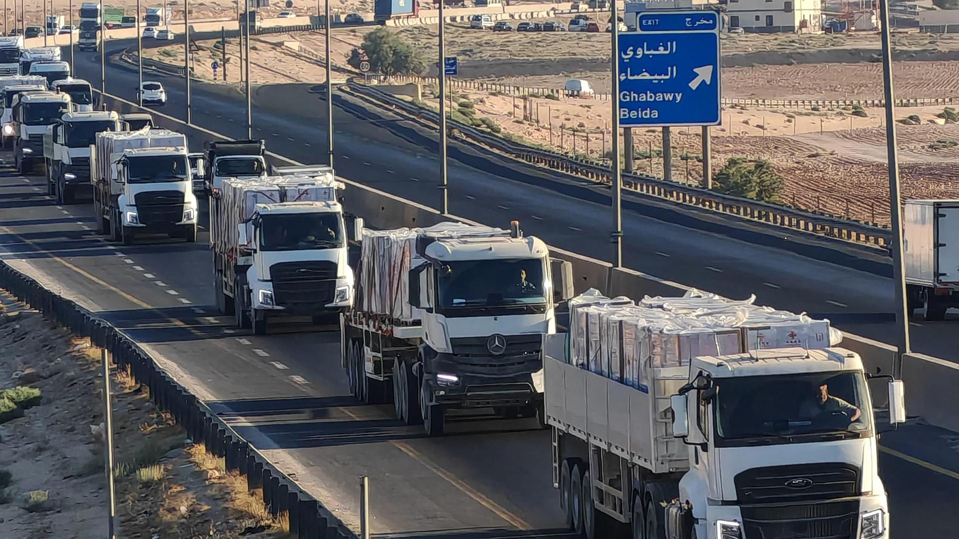 Mehrere LKW mit Hilfsgütern für den Gazastreifen fahren hintereinander auf einer Straße. 