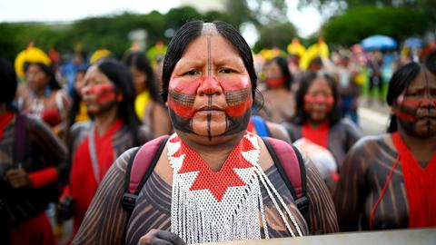 Eine indigene Frau steht an der Spitze einer Demonstration. Ihr Gesicht ist in traditionellen Farben bemalt.