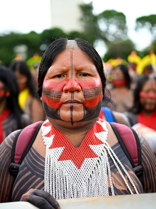Eine indigene Frau steht an der Spitze einer Demonstration. Ihr Gesicht ist in traditionellen Farben bemalt.