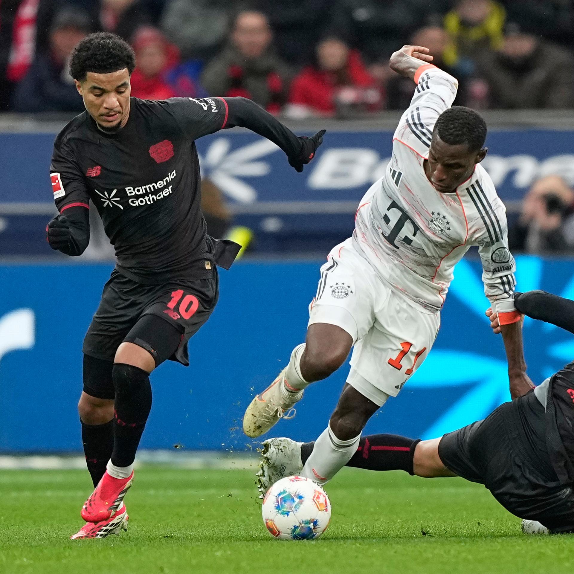 Bayern-Stürmer Nicolas Jackson (mi.) im Zweikampf mit den Leverklusenern Malik Tillman (l) und Equi Fernandez.