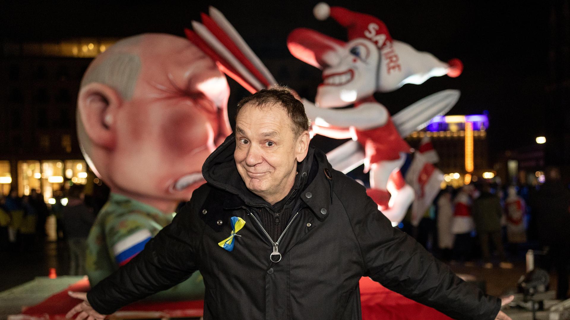 Der Künstler Jacques Tilly steht vor seinem Mottowagen "Putin spießt den Düsseldorfer Hoppeditz auf" bei einer Kundgebung auf dem Roncalliplatz in Köln anlässlich des Jahrestages des russischen Großangriffs auf die Ukraine.