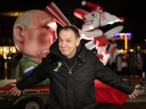 Der Künstler Jacques Tilly steht vor seinem Mottowagen "Putin spießt den Düsseldorfer Hoppeditz auf" bei einer Kundgebung auf dem Roncalliplatz in Köln anlässlich des Jahrestages des russischen Großangriffs auf die Ukraine.