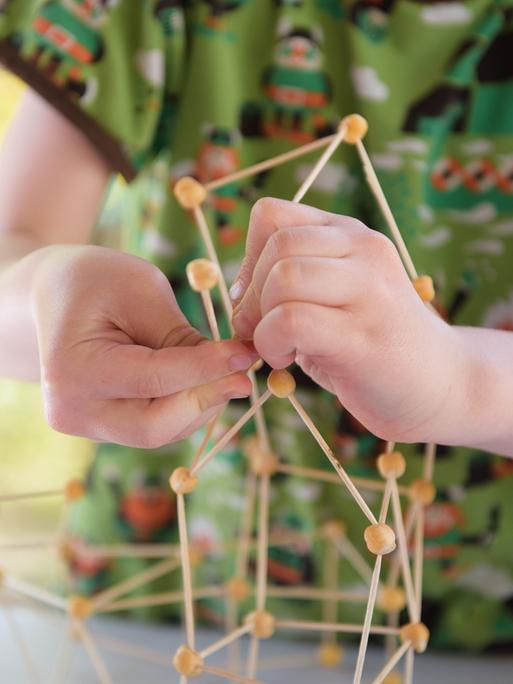 Ein Kind bastelt in einer Fröbel-Kita ein Modell aus Zahnstochern und Kichererbsen.