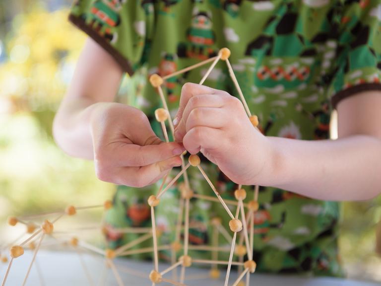 Ein Kind bastelt in einer Fröbel-Kita ein Modell aus Zahnstochern und Kichererbsen.