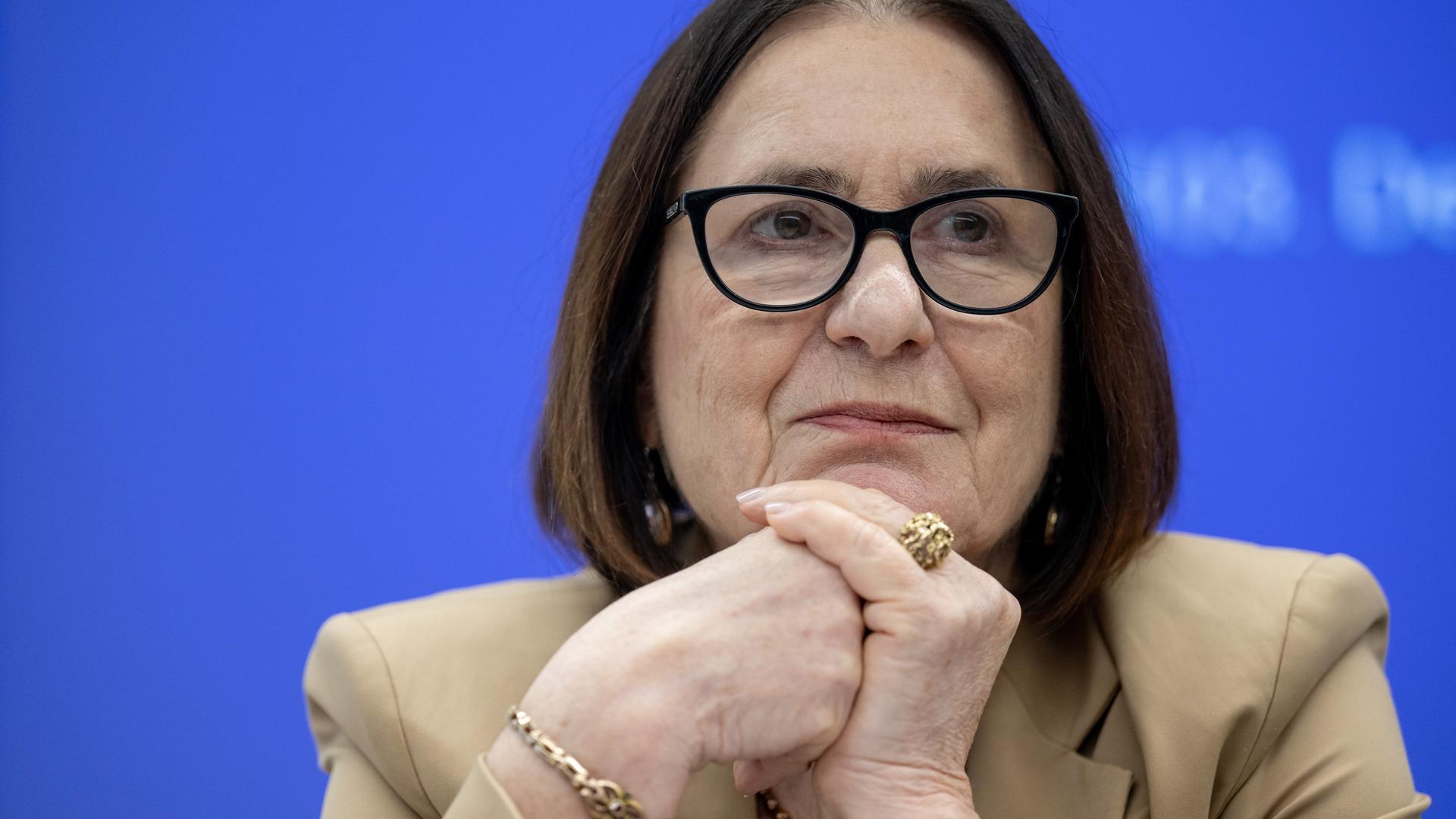 Irina Scherbakowa sitzt den Kopf auf die Hände gestützt vor einem blauen Hintergrund. Sie trägt einen großen goldenen Ring und eine schwarz umrandete Brille. Irina Scherbakowa sitzt den Kopf auf die Hände gestützt vor einem blauen Hintergrund. Sie trägt einen großen goldenen Ring und eine schwarz umrandete Brille.