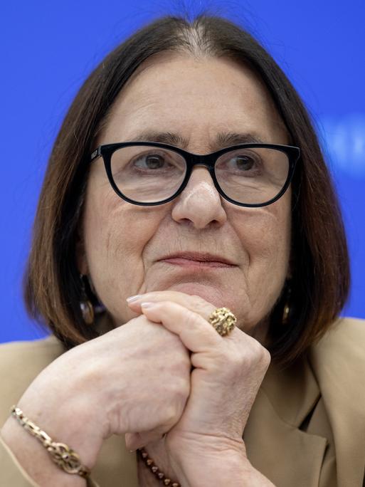 Irina Scherbakowa sitzt den Kopf auf die Hände gestützt vor einem blauen Hintergrund. Sie trägt einen großen goldenen Ring und eine schwarz umrandete Brille.