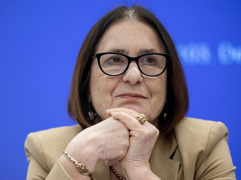 Irina Scherbakowa sitzt den Kopf auf die Hände gestützt vor einem blauen Hintergrund. Sie trägt einen großen goldenen Ring und eine schwarz umrandete Brille.