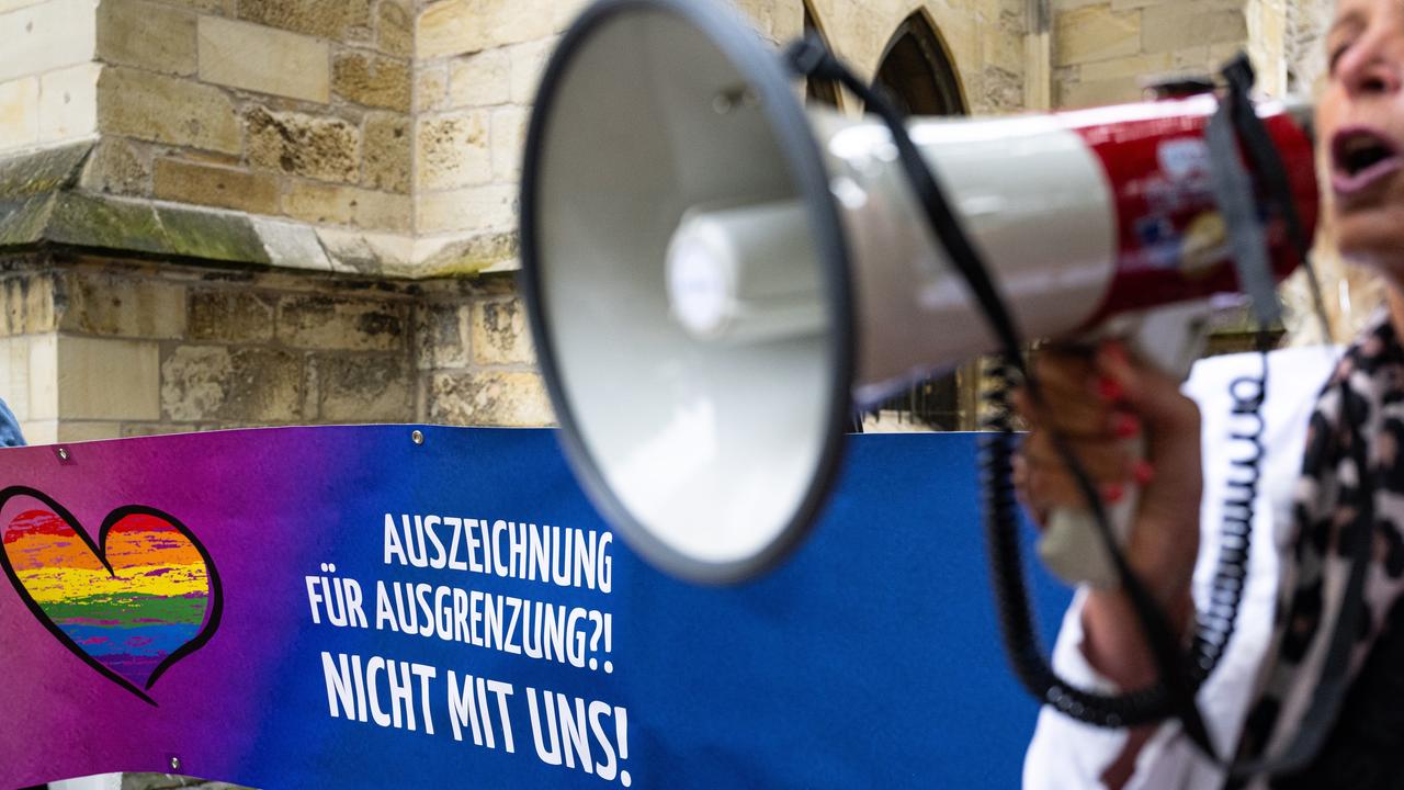 Auf einem Transparent steht "Auszeichnung für Ausgrenzung?! Nicht mit uns!"  Eine Frau steht daneben und ruft etwas in ein Megafon.