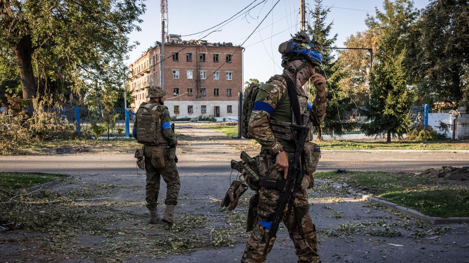 Auf einer Strasse vor einem rötlichen Gebäude stehen in der russischen Region Kursk zwei ukrainische Soldaten auf der Strasse.