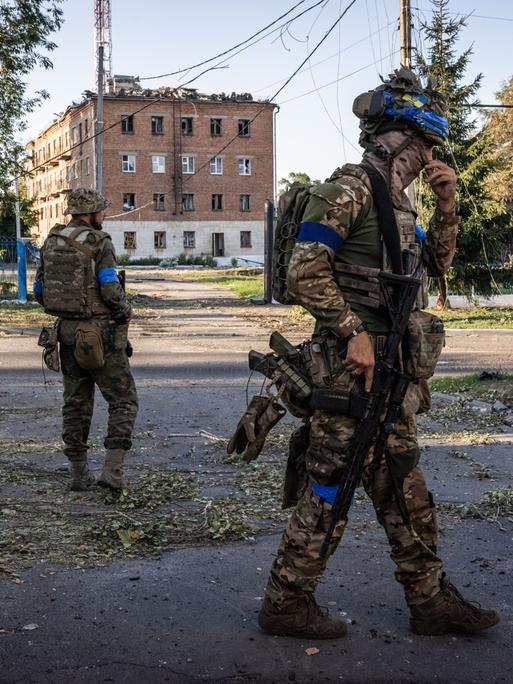 Auf einer Strasse vor einem rötlichen Gebäude stehen in der russischen Region Kursk zwei ukrainische Soldaten auf der Strasse.