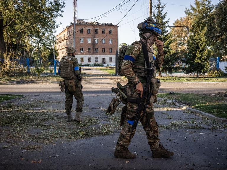 Auf einer Strasse vor einem rötlichen Gebäude stehen in der russischen Region Kursk zwei ukrainische Soldaten auf der Strasse.