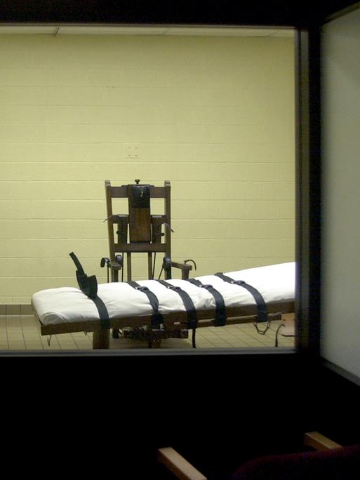 Blick vom Zeugenraum aus in die Hinrichtungskammer einer amerikanischen Justizvollzugsanstalt, in der sich ein Stuhl und eine Liege mit Gurten befindet. Blick vom Zeugenraum aus in die Hinrichtungskammer einer amerikanischen Justizvollzugsanstalt, in der sich ein Stuhl und eine Liege mit Gurten befindet.