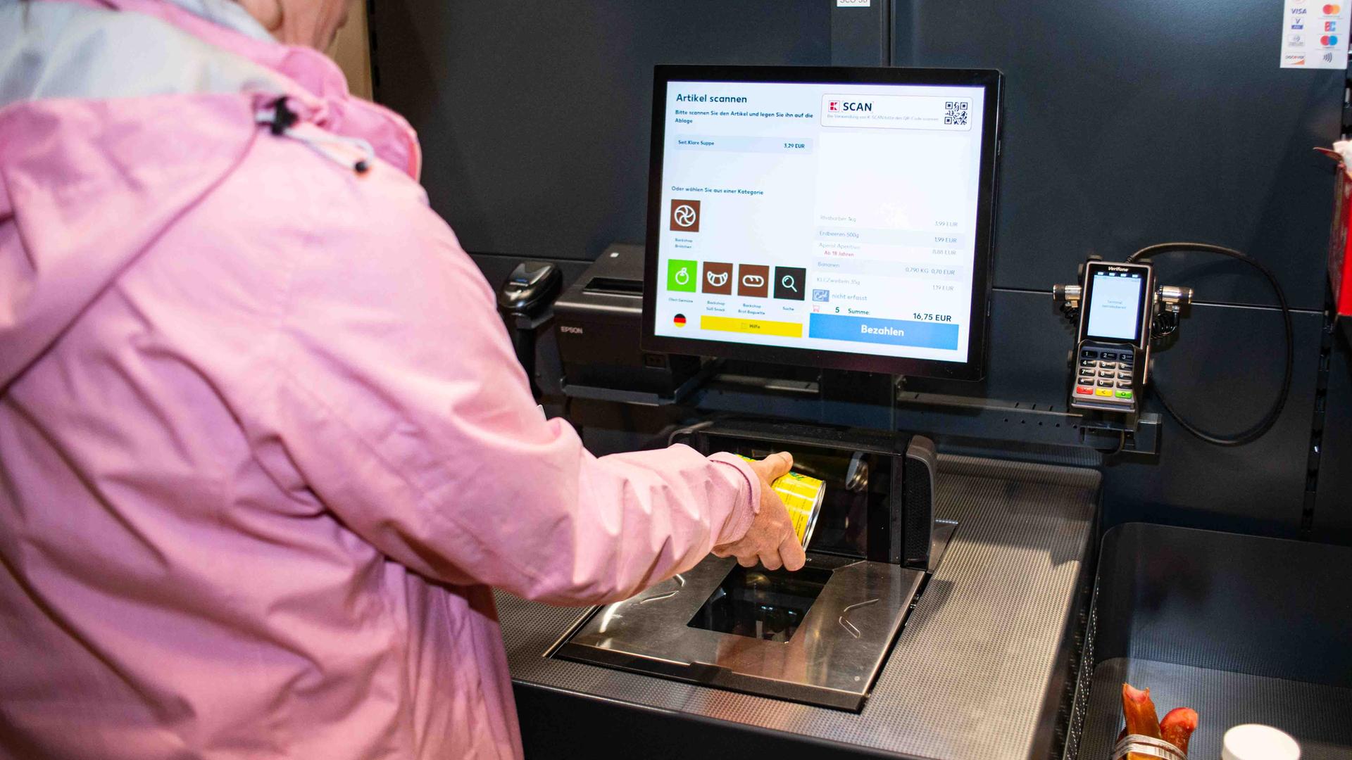 Eine Kundin probiert die SB-Kasse aus und hält Ware an den Scanner. Eine Kundin probiert die SB-Kasse aus und hält Ware an den Scanner.