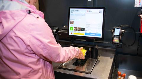 Eine Kundin probiert die SB-Kasse aus und hält Ware an den Scanner.