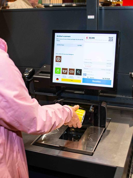 Eine Kundin probiert die SB-Kasse aus und hält Ware an den Scanner.