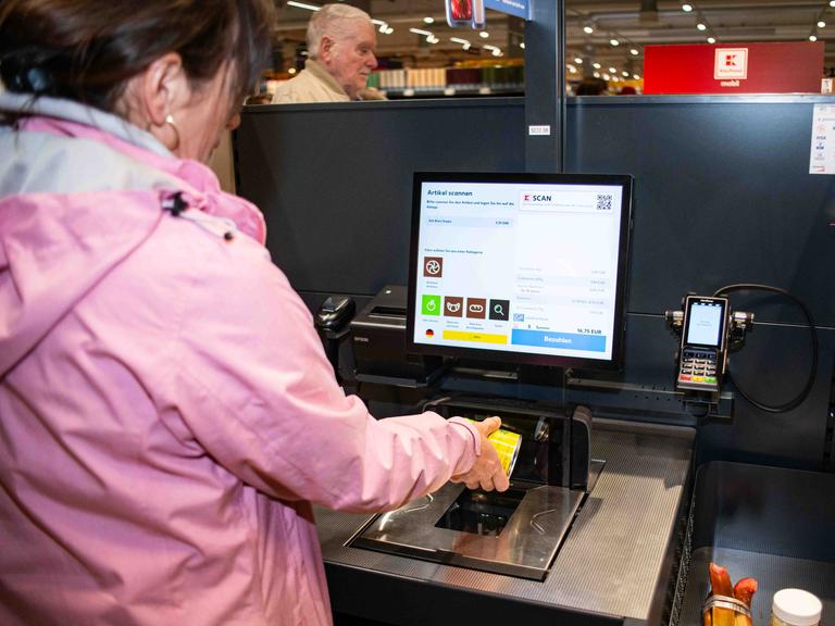 Eine Kundin probiert die SB-Kasse aus und hält Ware an den Scanner.