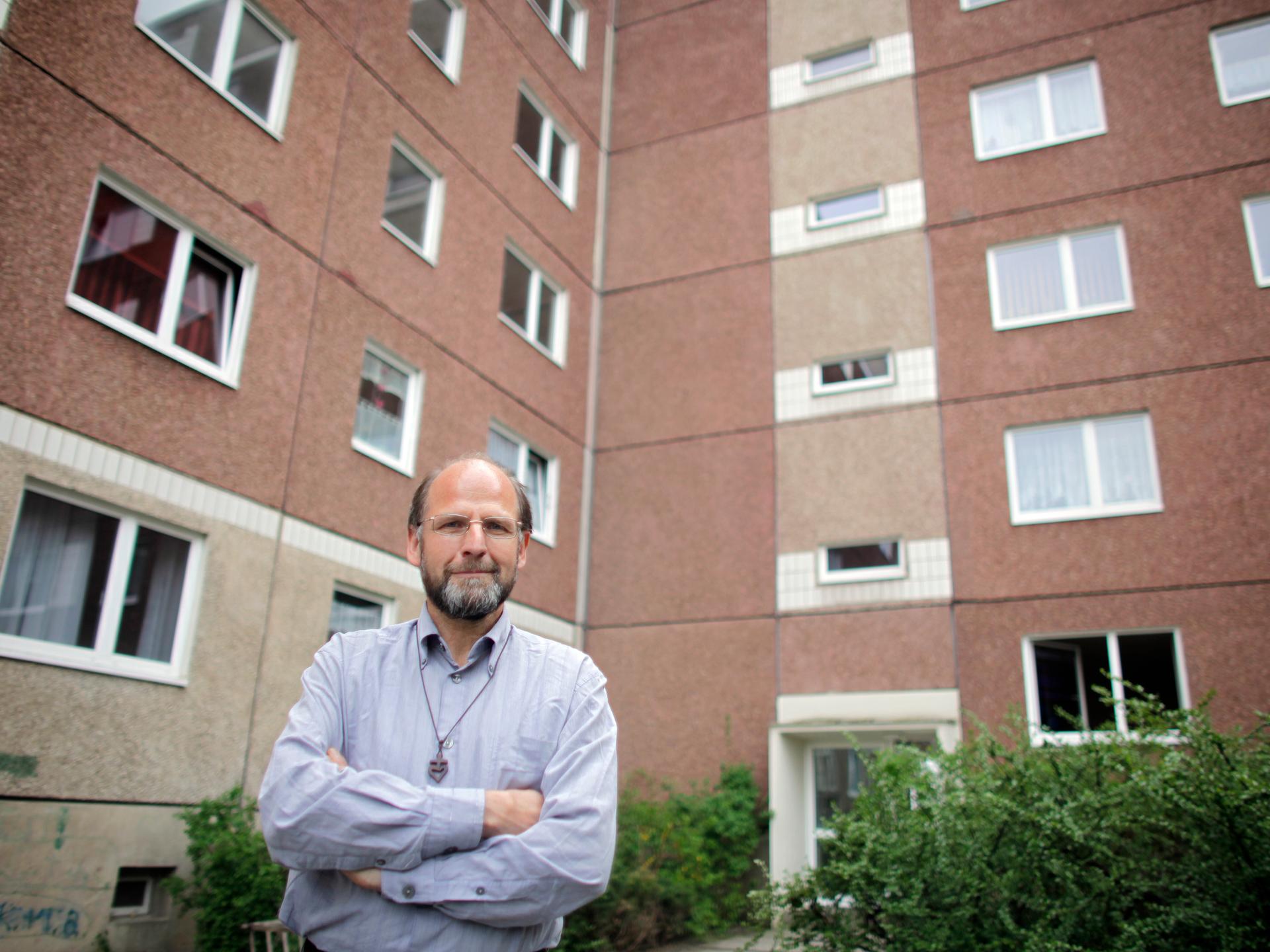 Bruder Andreas vom katholischen Orden der "Kleinen Brüder vom Evangelium" steht vor einem DDR-Plattenbau-Wohnhaus in Leipzig-Grünau.