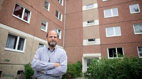 Bruder Andreas vom katholischen Orden der "Kleinen Brüder vom Evangelium" steht vor einem DDR-Plattenbau-Wohnhaus in Leipzig-Grünau.