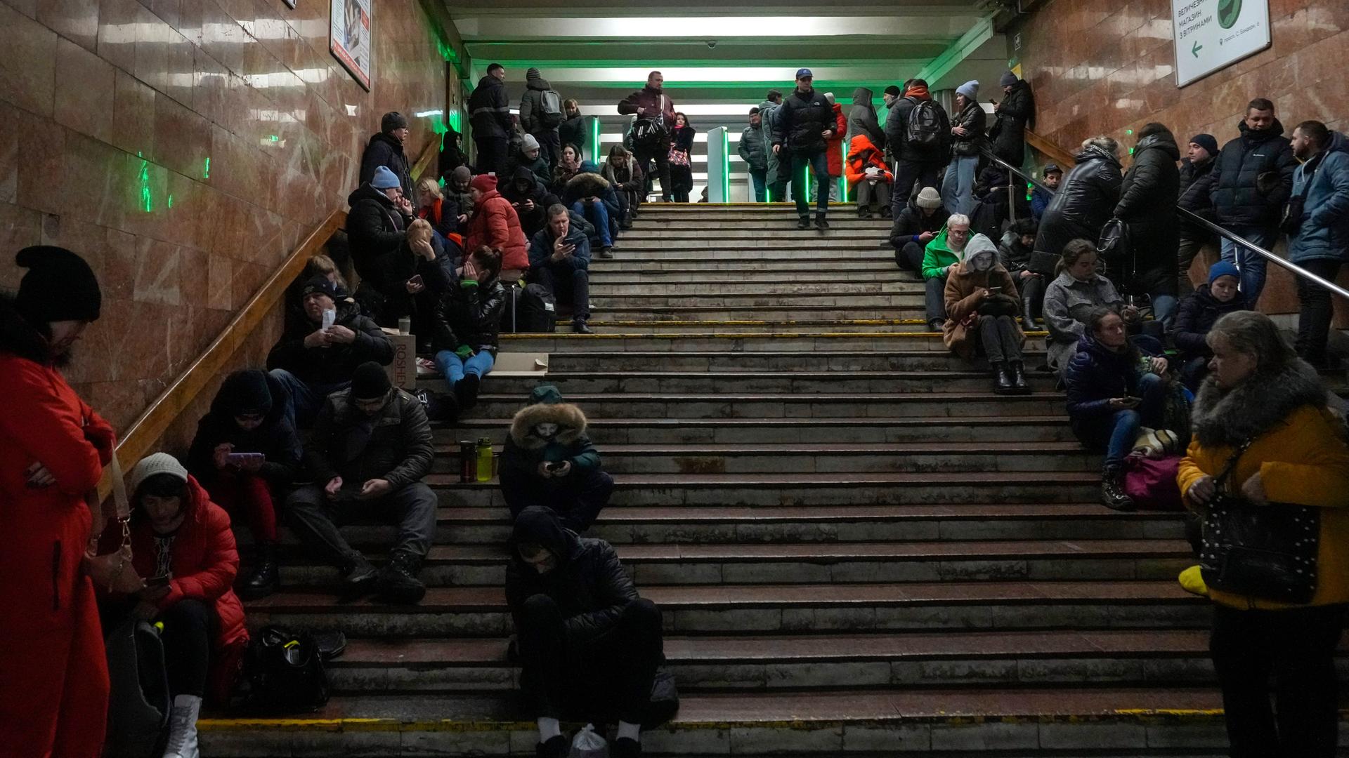 Menschen sitzen in Kiew auf Treppen in einer U-Bahn-Station, die während eines Raketenangriffs als Luftschutzbunker genutzt wird.