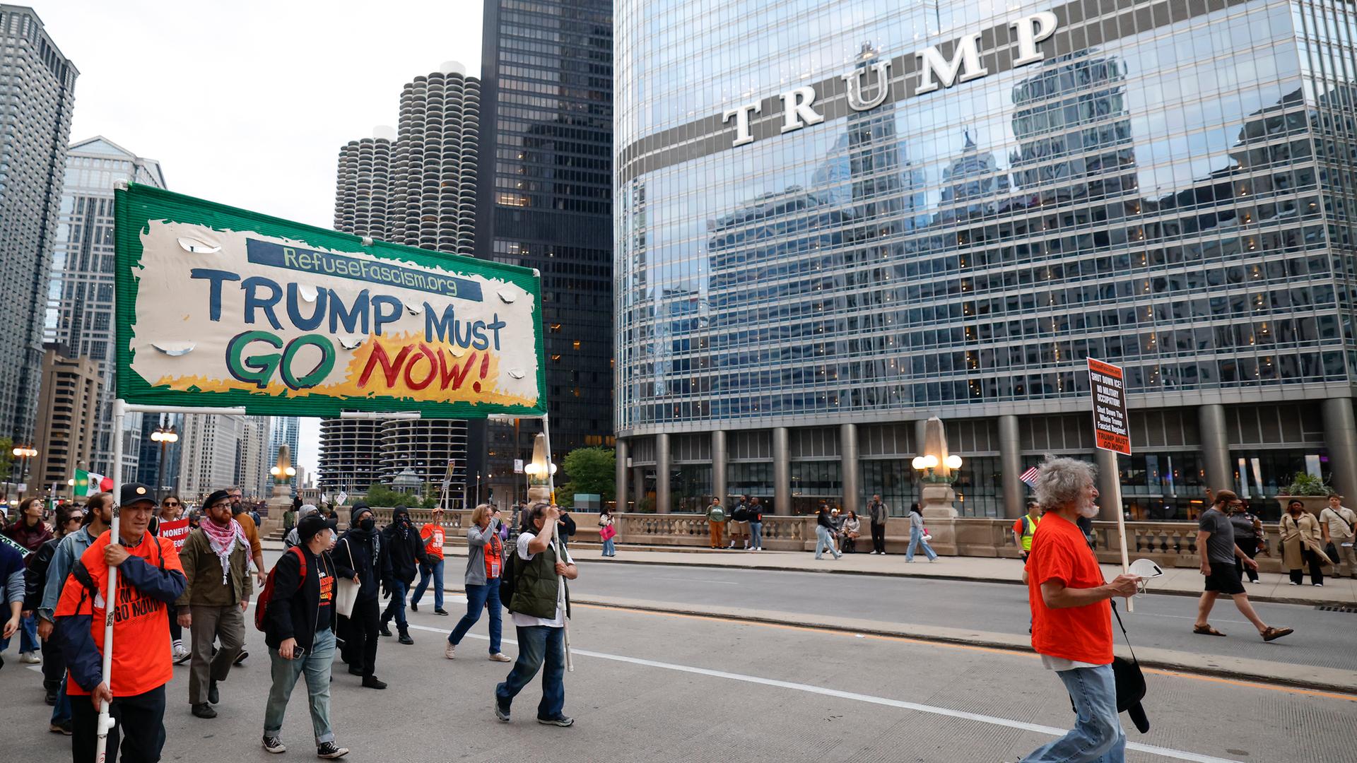 Eine Gruppe Demonstranten vor dem Trump Tower in Chicago trägt ein Transparent mit der Aufschrift "Trump must go now" - Trump muss sofort gehen! Eine Gruppe Demonstranten vor dem Trump Tower in Chicago trägt ein Transparent mit der Aufschrift "Trump must go now" - Trump muss sofort gehen!