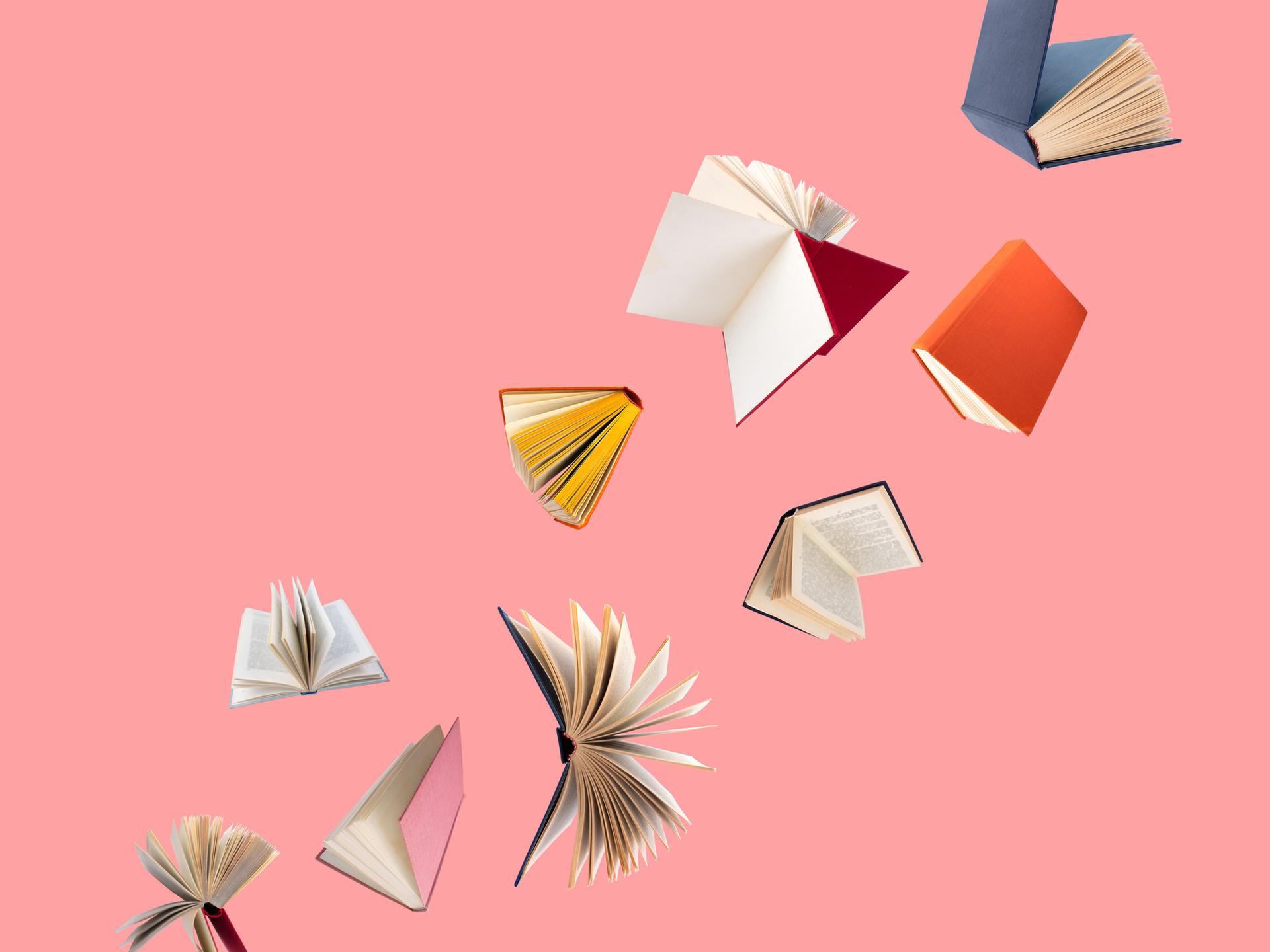 Farbig bezogene Bücher fliegen vor einem rosa Hintergrund durch die Luft. Farbig bezogene Bücher fliegen vor einem rosa Hintergrund durch die Luft.