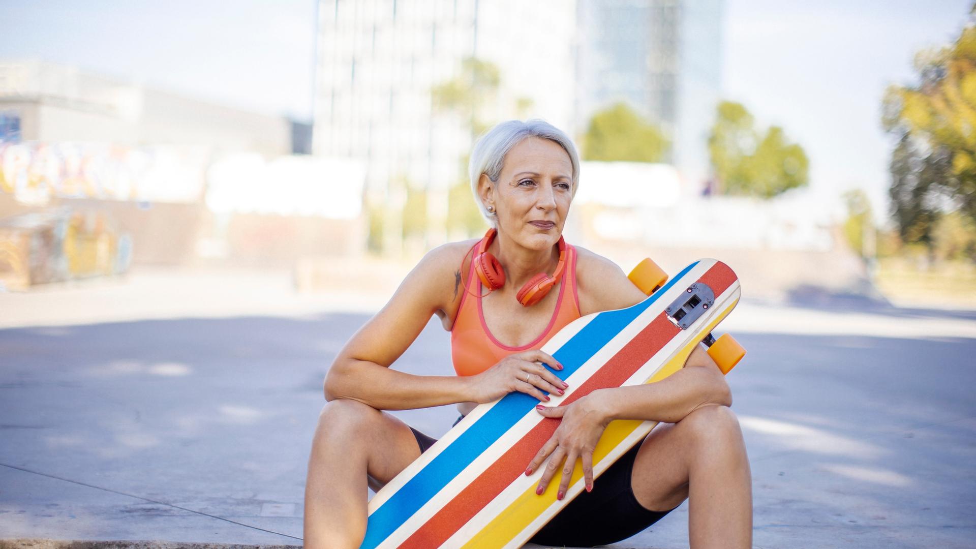 Ältere Frau, die ihre Freizeit genießt, während sie in Sportkleidung und mit Kopfhörern im Park Skateboard fährt.
