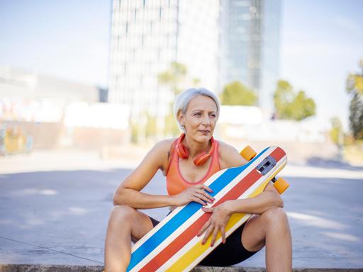 Ältere Frau, die ihre Freizeit genießt, während sie in Sportkleidung und mit Kopfhörern im Park Skateboard fährt.