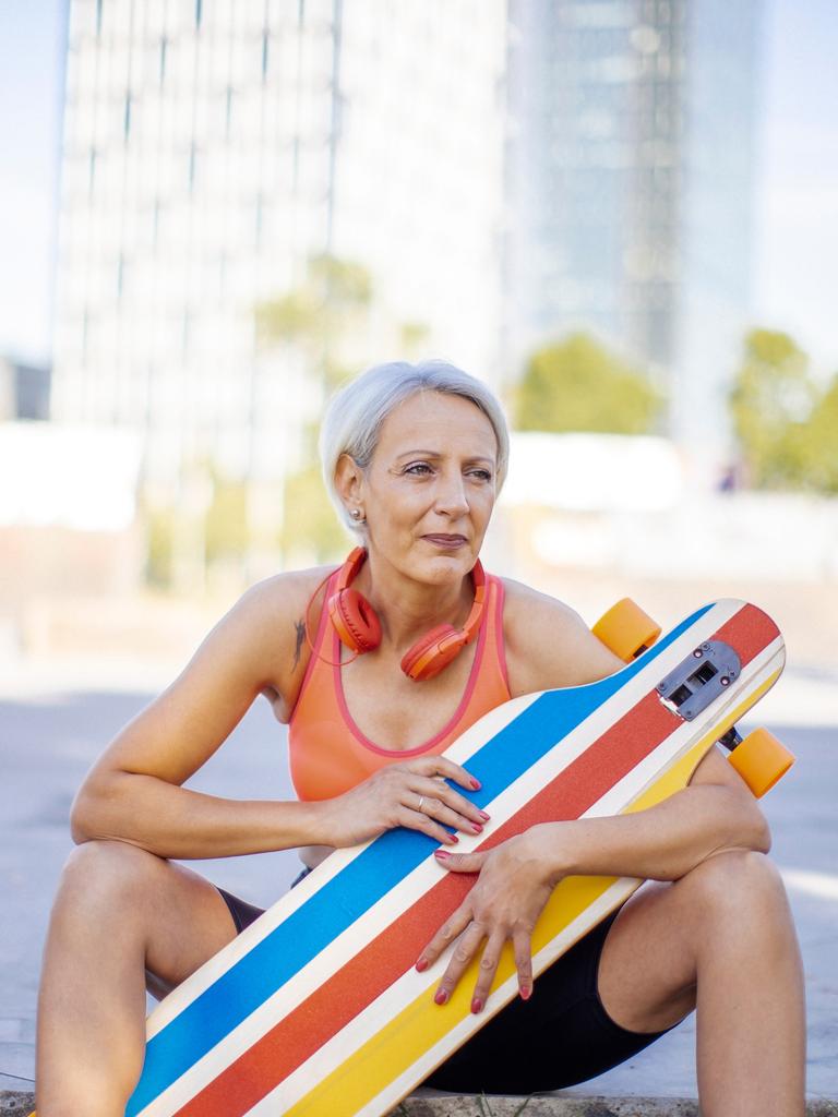 Ältere Frau, die ihre Freizeit genießt, während sie in Sportkleidung und mit Kopfhörern im Park Skateboard fährt.