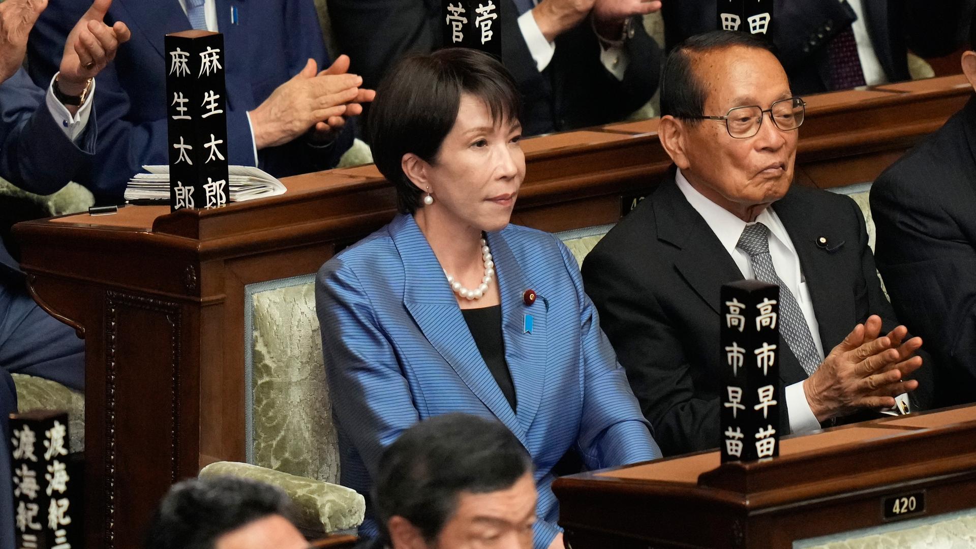 Sanae Takaichi sitzt im Parlament zwischen den Abgeordneten, die ihr applaudieren. Sanae Takaichi sitzt im Parlament zwischen den Abgeordneten, die ihr applaudieren.