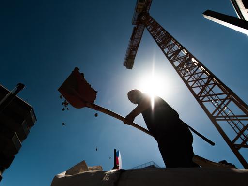 Ein Bauarbeiter arbeitet mit einer Schaufel, die Sonne scheint vom Himmel.