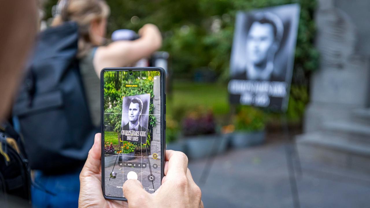 Das Foto zeigt eine Hand, die ein Handy hält und ein Gedenkfoto von Charlie Kirk fotografiert
