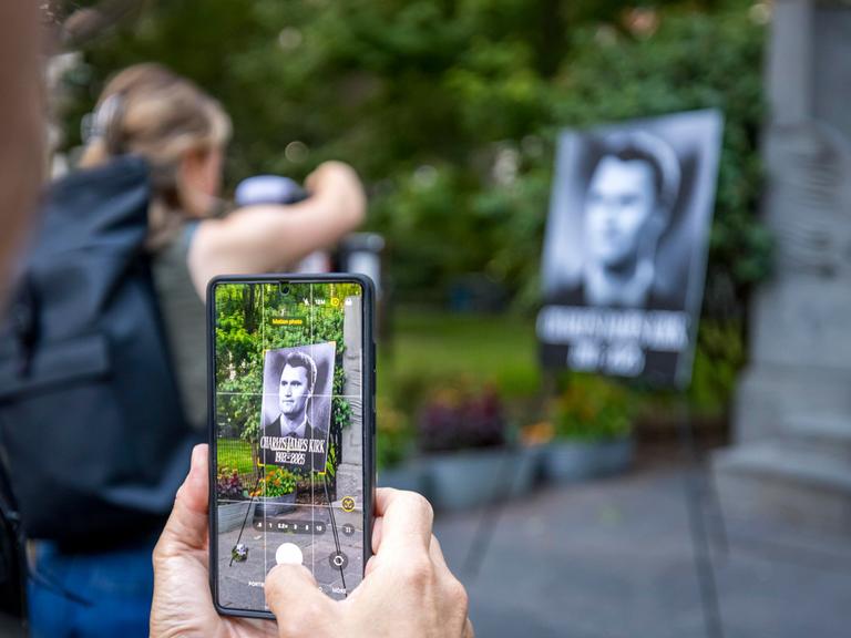 Das Foto zeigt eine Hand, die ein Handy hält und ein Gedenkfoto von Charlie Kirk fotografiert