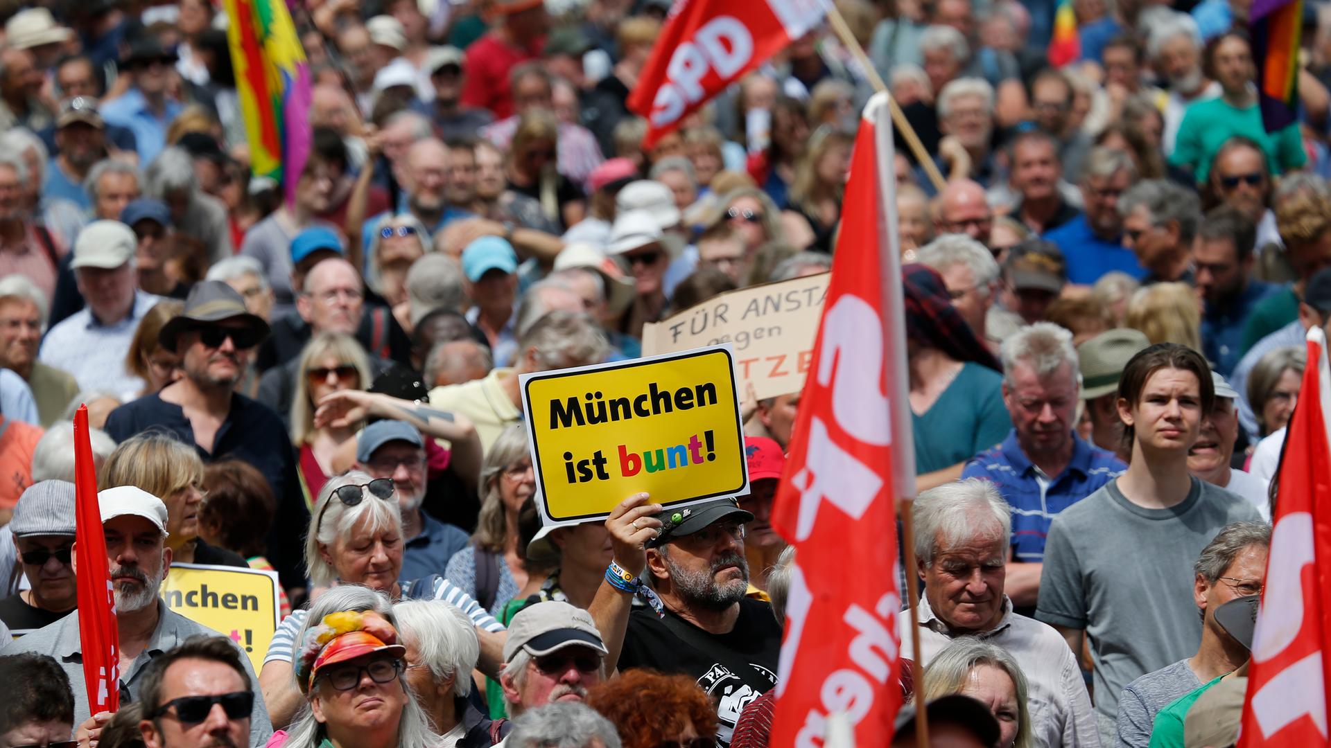 Bei einer Demonstration wird ein Schild mit dem Logo des Vereins "München ist bunt" hochgehalten.