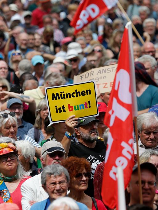 Bei einer Demonstration wird ein Schild mit dem Logo des Vereins "München ist bunt" hochgehalten.