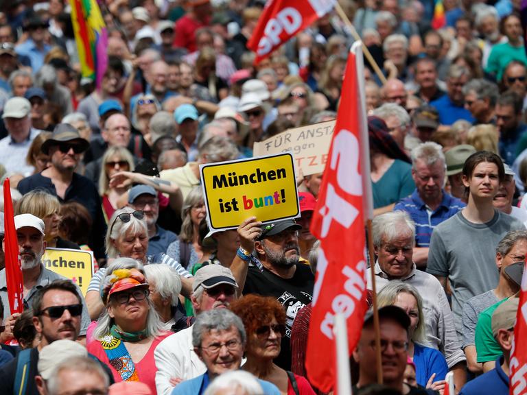 Bei einer Demonstration wird ein Schild mit dem Logo des Vereins "München ist bunt" hochgehalten.