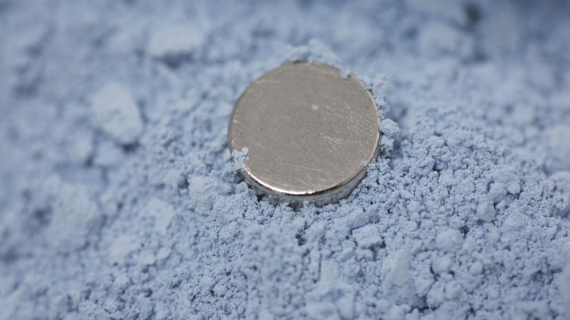 Die pulverförmige bläuliche Seltene Erde Neodymoxid. Darin liegt ein runder Magnet.