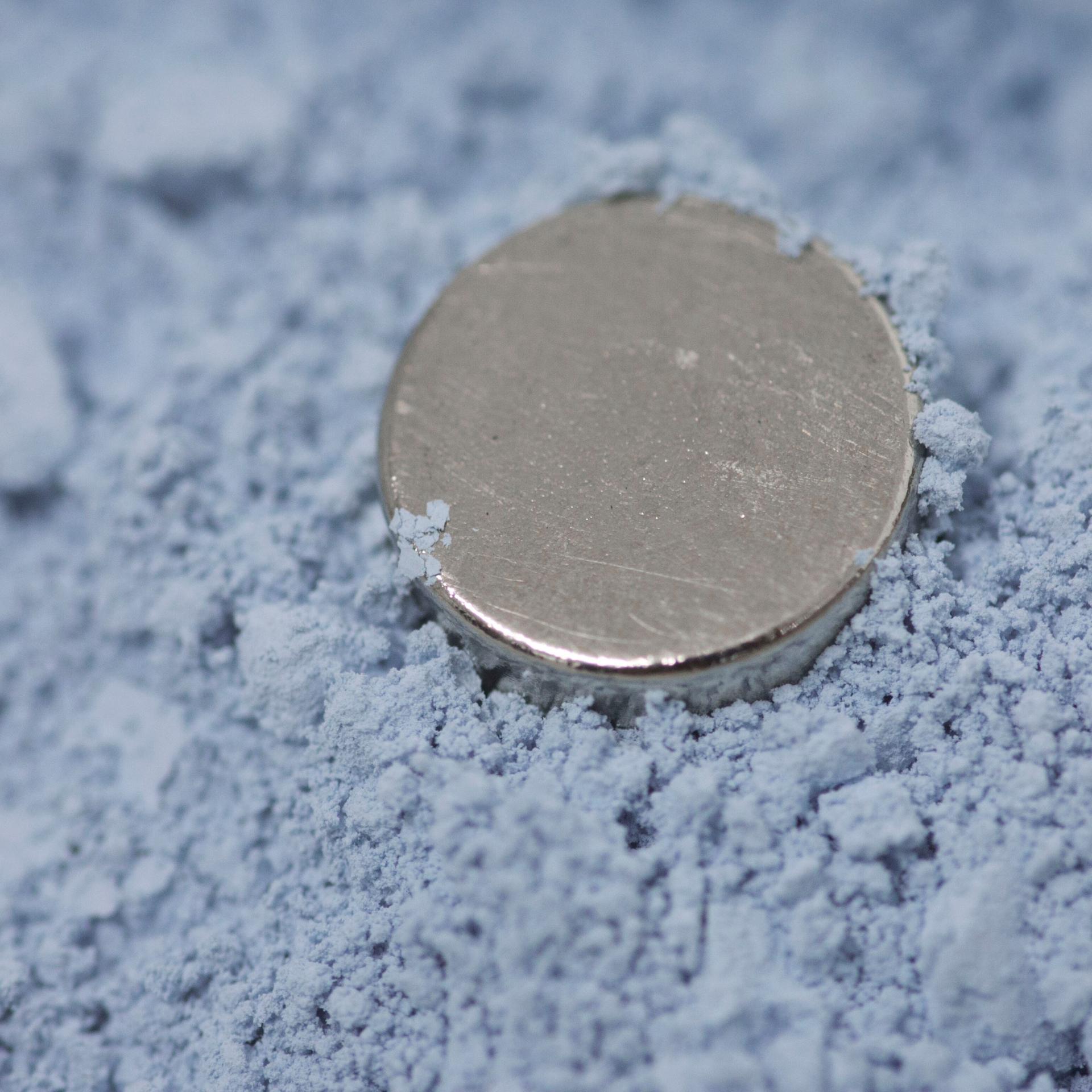 Die pulverförmige bläuliche Seltene Erde Neodymoxid. Darin liegt ein runder Magnet.