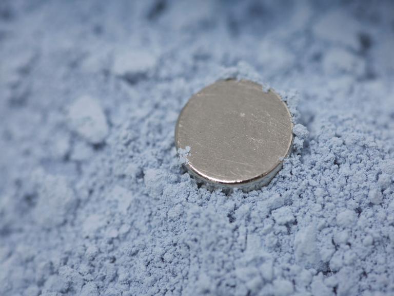Die pulverförmige bläuliche Seltene Erde Neodymoxid. Darin liegt ein runder Magnet.