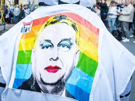 Ein Demonstrant in Budapest trägt eine Shirt, auf dessen Rücken Viktor Orbán in Regenbogenfarben zu sehen ist.