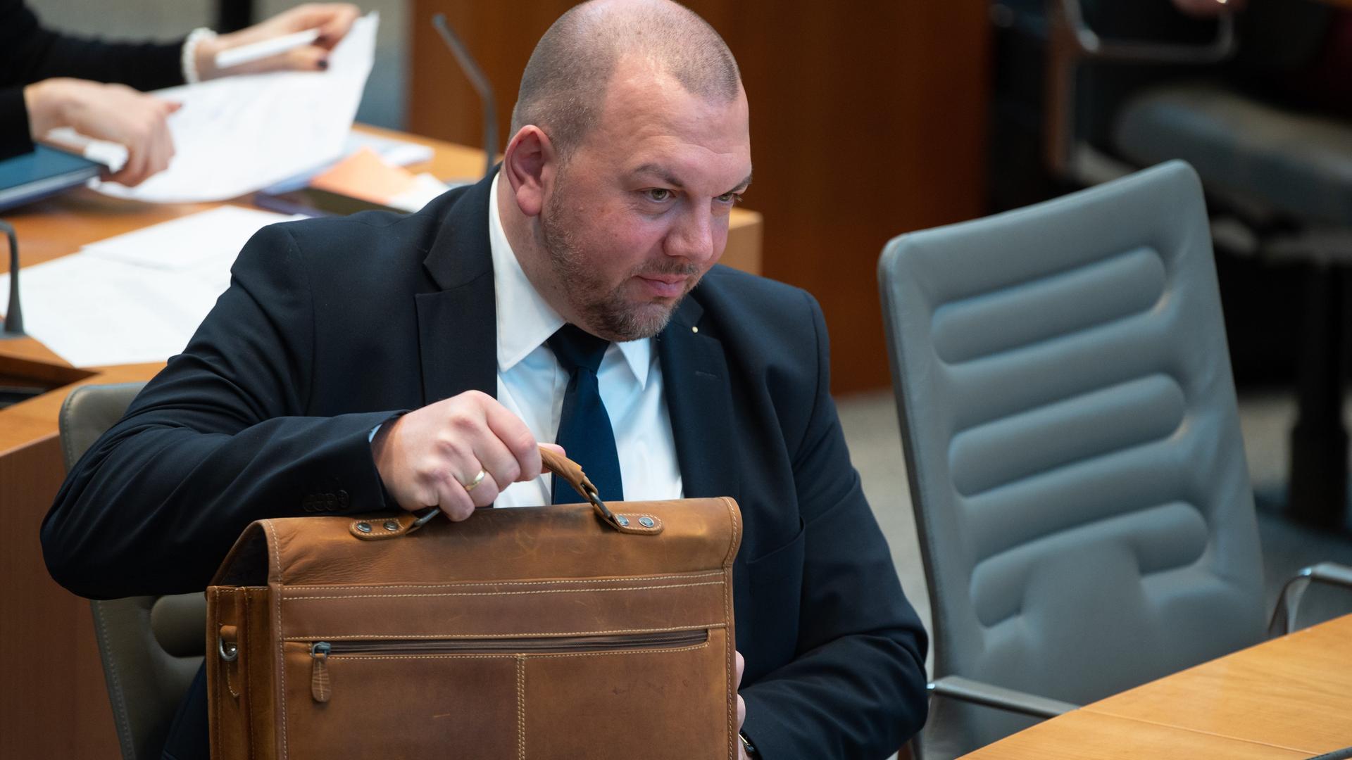 Esser erhebt sich von seinem Sitzplatz im Parlament und hebt dabei seine Aktentasche hoch