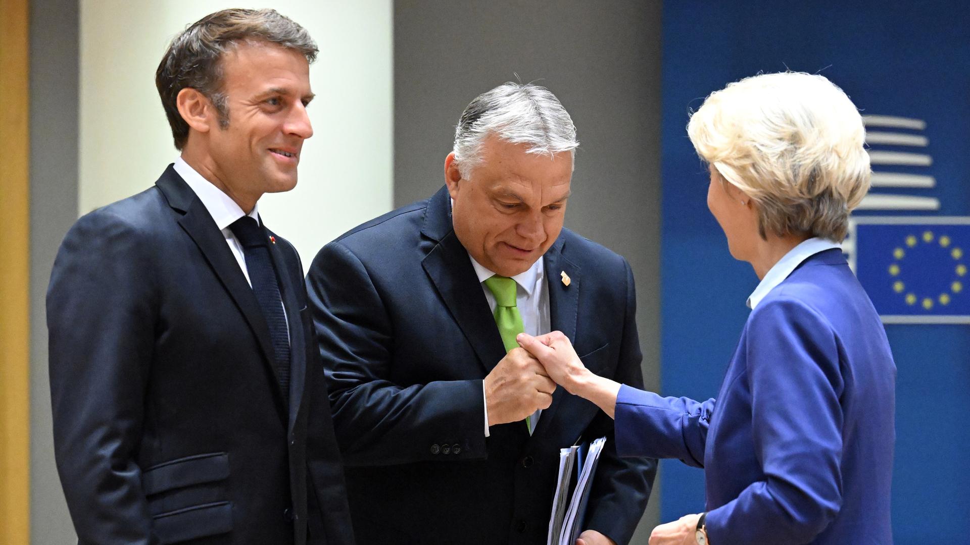 EU-Kommissionspräsidentin Ursula von der Leyen (r) und und der ungarische Ministerpräsident Viktor Orban (m) schütteln sich die Hände, der französische Staatspräsident Emmanuel Macron (l) steht daneben.
