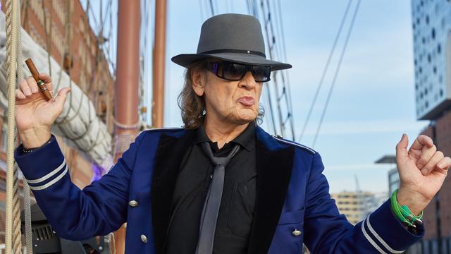 Der Musiker Udo Lindenberg steht mit ausgebreiteten Armen auf auf einem Segel-Schiff neben der Elbphilharmonie in Hamburg. 