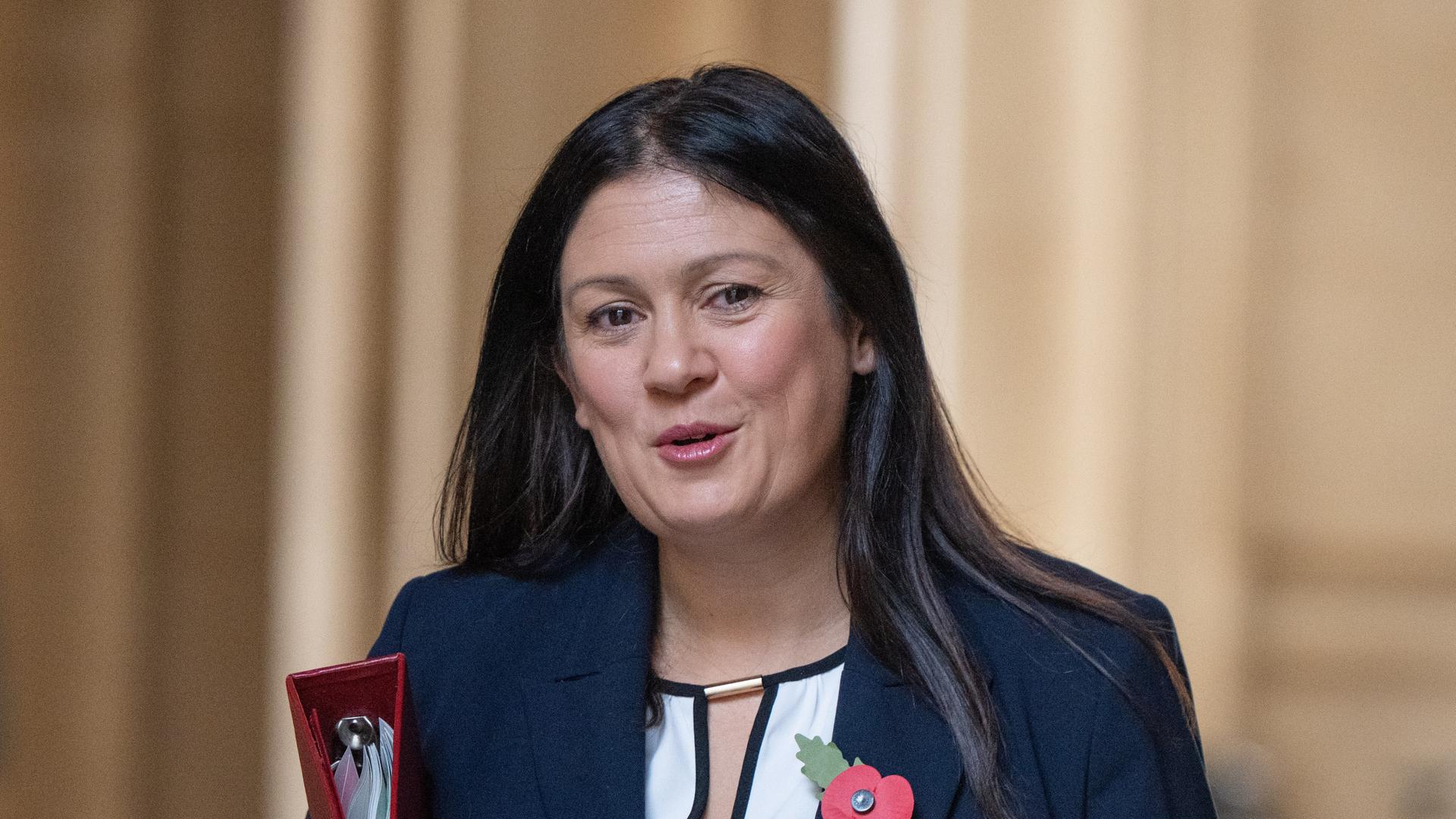 Großbritanniens Kulturministerin Lisa Nandy lächelt in die Kamera. Sie trägt eine Blatt und Apfel-Brosche und unter dem Arm einen Aktenordner Großbritanniens Kulturministerin Lisa Nandy lächelt in die Kamera. Sie trägt eine Blatt und Apfel-Brosche und unter dem Arm einen Aktenordner